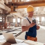 Cheerful builder using smartphone at construction site