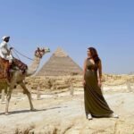 A man riding a camel and a woman having a picture to the pyramid of Giza as background — one of Egypt Bucket List.