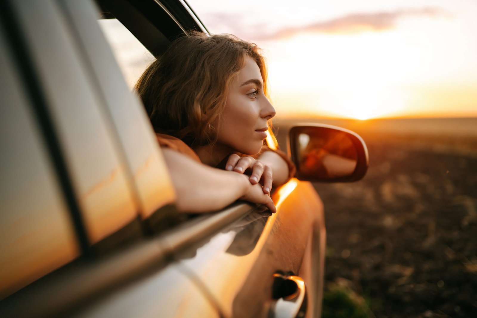 Happy woman outstretches her arms while sticking out car window. Lifestyle, travel, tourism, nature.