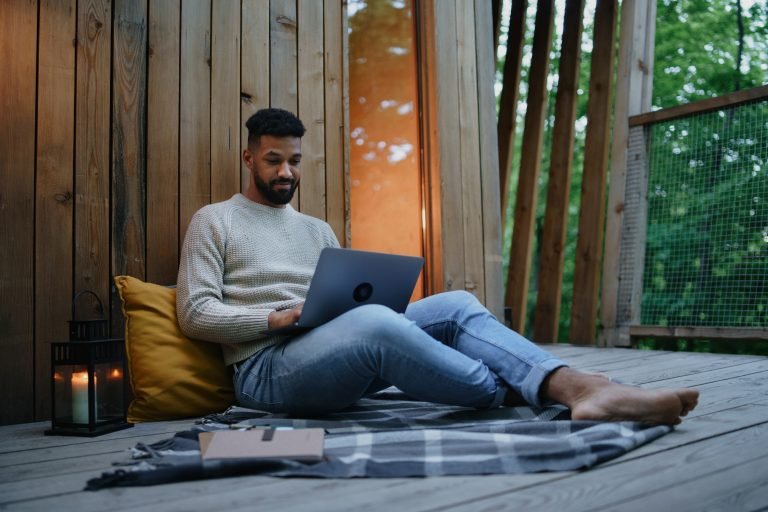 Man with laptop resting outdoors in a tree house, weekend away and remote office concept.