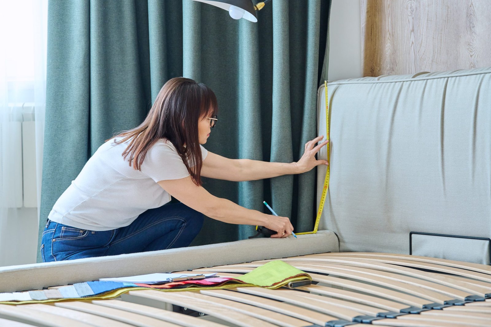 Woman textile designer with tape measure measuring size of bed in bedroom