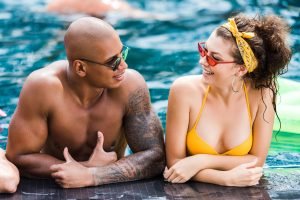 young in sunglasses looking at each other in swimming pool
