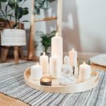 Feng Shui wooden tray with burning candles and white Buddha statuette on the floor of modern interior.