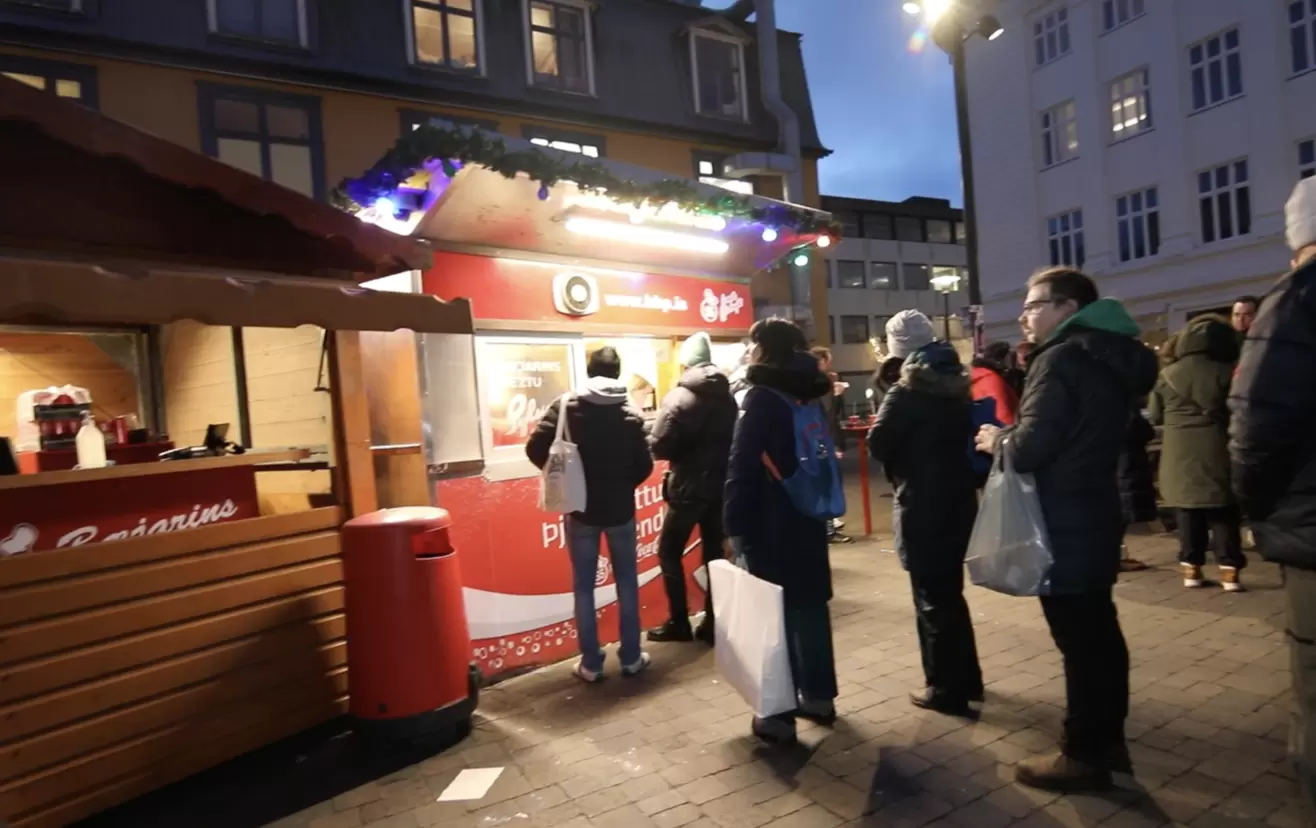 a group of people standing in front of a hotdog food stand in Reykjavik Iceland.