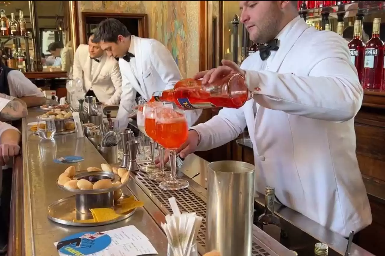 a group of men in white jackets pouring campari drinks into glasses in Milan.