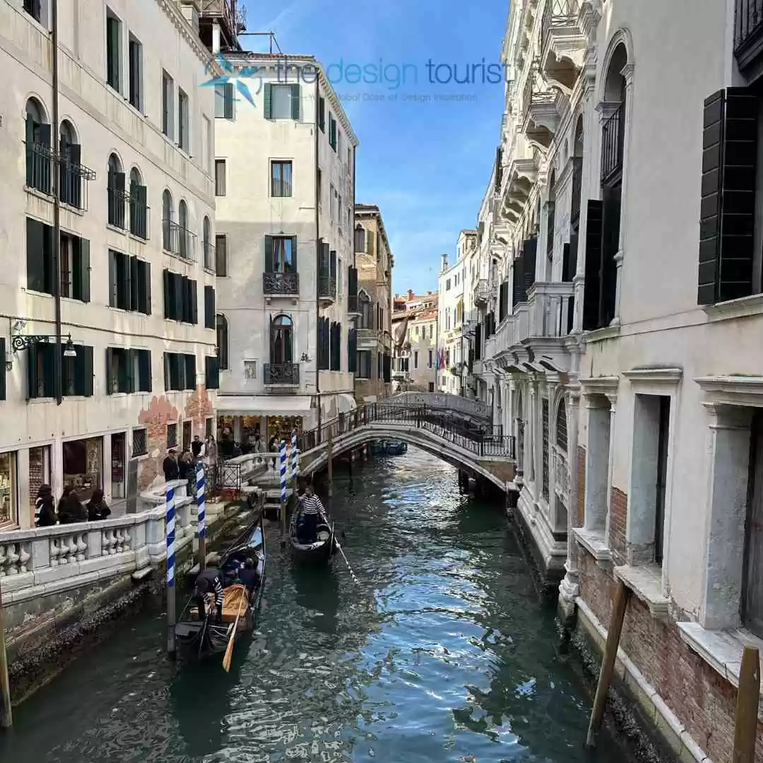 7 Must-Do Activities in Venice, Italy for an Unforgettable Trip A black, elongated gondola with a curved cabin navigates a calm canal in Venice, Italy. Buildings with colorful facades line the canal's edge.