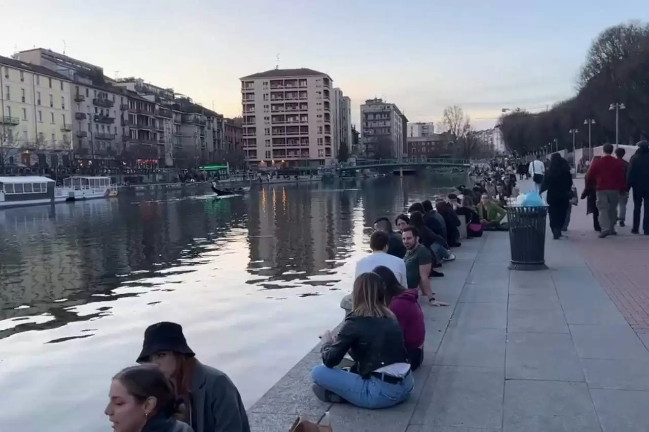 a group of people sitting on the side of navigli canal in Milan Italy
