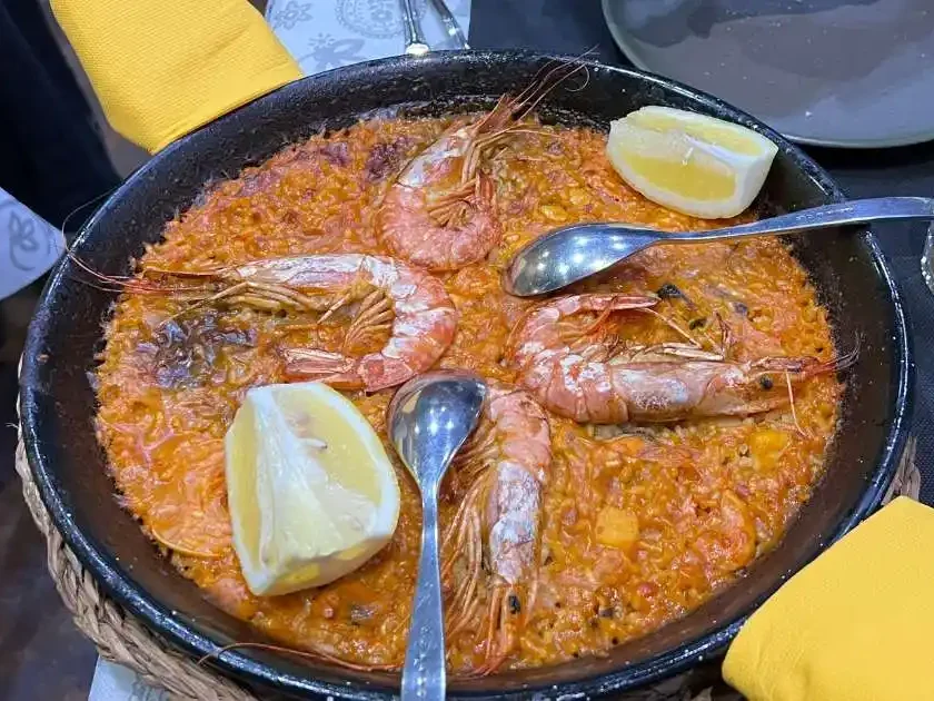 a pan of paella food with shrimp and lemon slices