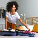 Happy African American young woman packing suitcase at home. Preparing for summer holidays abroad.