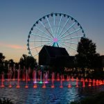 Ferris wheel and water fountain with colored lights at dusk