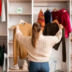 A woman choosing her outfit in a wardrobe with words 5 Winter Fashion Essentials Every Woman Should Have.