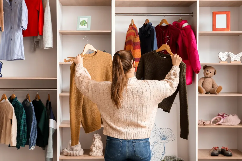 A woman choosing her outfit in a wardrobe with words 5 Winter Fashion Essentials Every Woman Should Have.