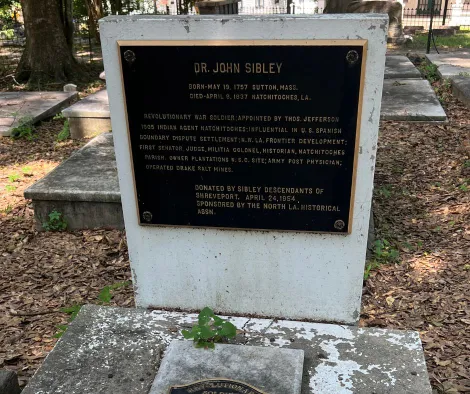 a plaque on the ground in front of a cemetery with words Dr. John Sibley.