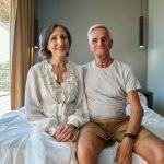Aged spouses on double bed staring at camera