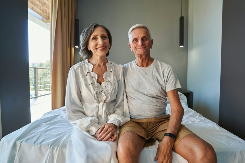 Aged spouses on double bed staring at camera