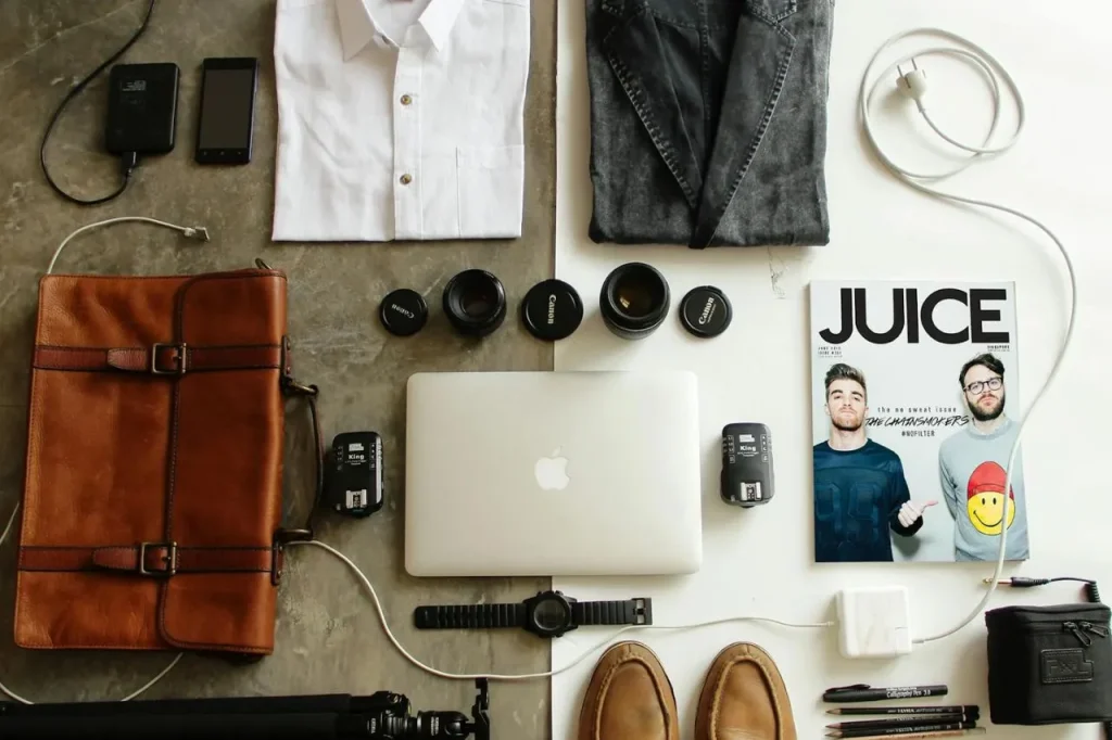 a table topped with a laptop computer next to a magazine and folded clothes.