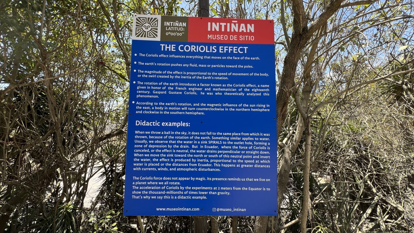 Informational sign about the Coriolis Effect at the Intiñan Museum, surrounded by trees and bushes.