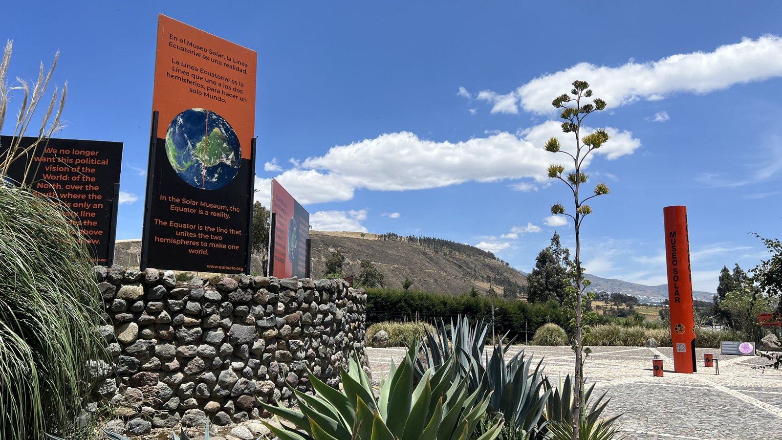 Outdoor exhibit at the Solar Museum with signs about the Equator, stone walls, agave plants, and a mountainous backdrop under a blue sky.