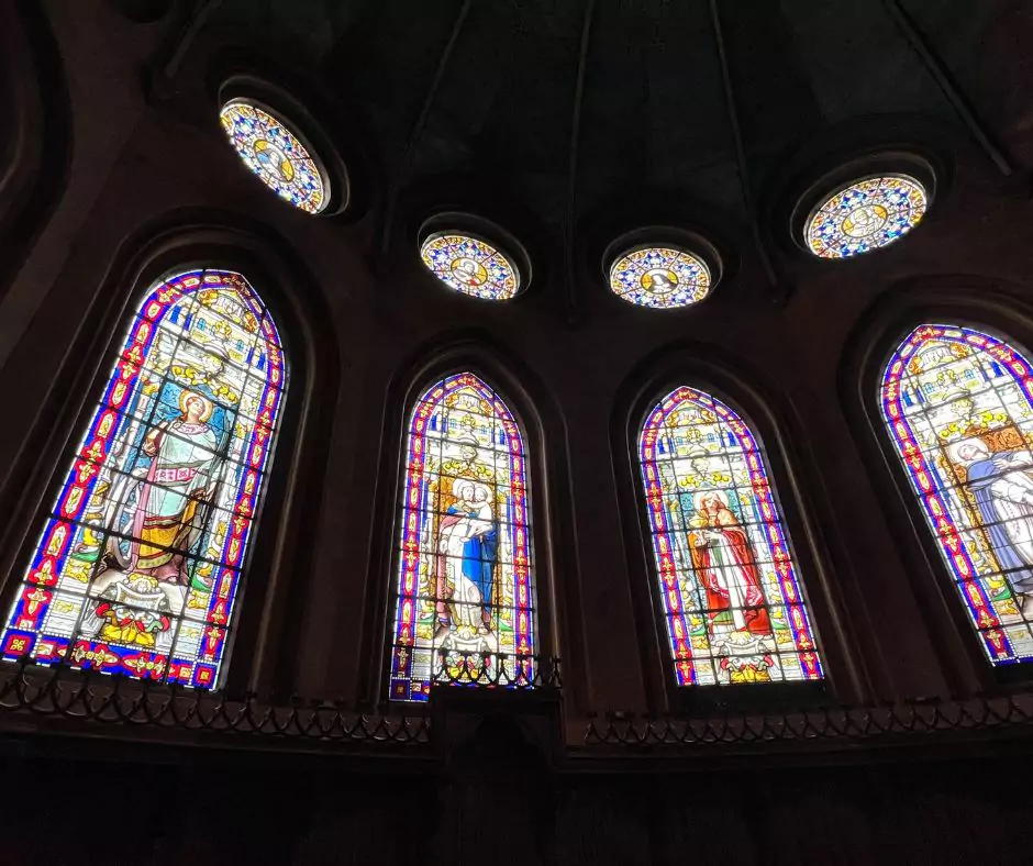 A row of vibrant stained-glass windows inside the Santo Domingo Convent in Quito, Ecuador, depicting detailed biblical scenes and saints framed by gothic arches and radiant colors.