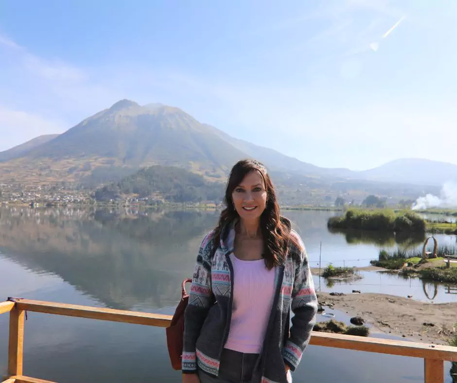 a woman standing in front of a lake with mountains in the background