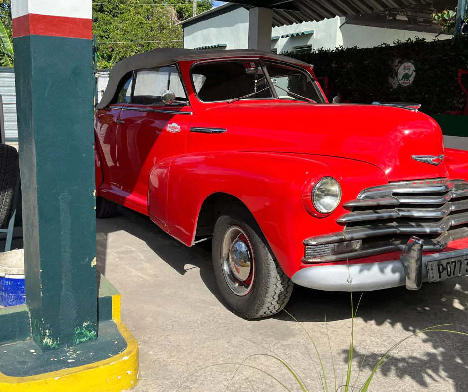 Red 1951 Chevrolet convertible with chrome grille and soft-top roof, parked at a vintage-style garage in Cuba.
