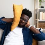 Distressed African American man covering ears because of loud noises.