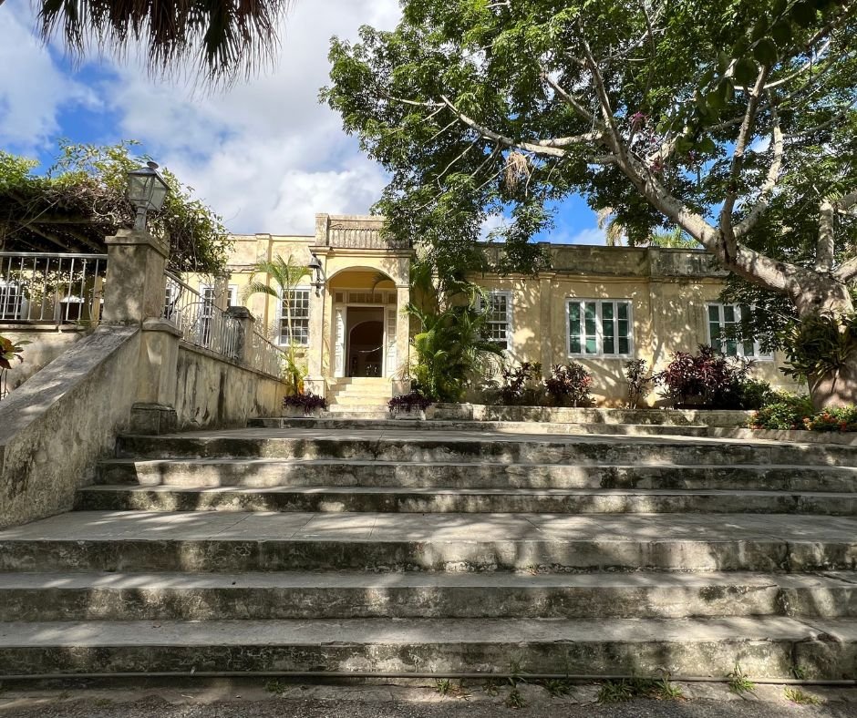 Finca Vigía exterior – Ernest Hemingway’s historic Cuban home, featuring a yellow facade, grand stone steps, lush greenery, and large windows.