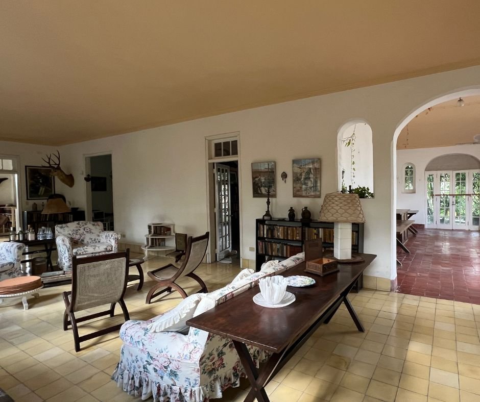 Finca Vigía living room – Spacious room with vintage floral furniture, bookshelves, and arched doorways leading to a dining area.