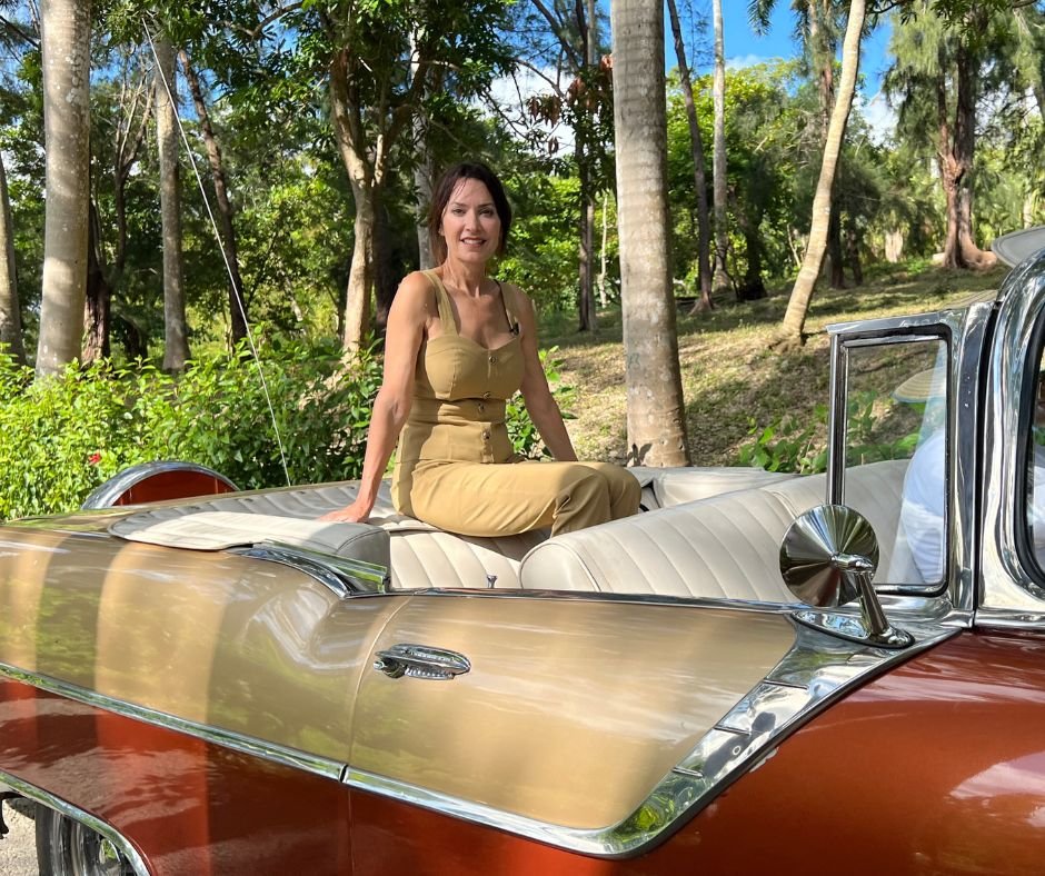 Classic convertible in Cuba – A woman in a tan outfit sitting on the back of a vintage car with a lush, tropical background.