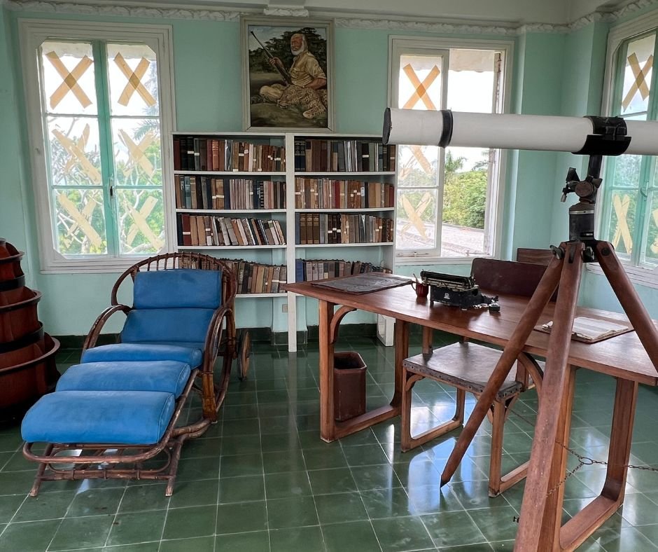 Hemingway’s study – A writing space with bookshelves, a wooden desk, a telescope, a typewriter, and a lounge chair, surrounded by windows.