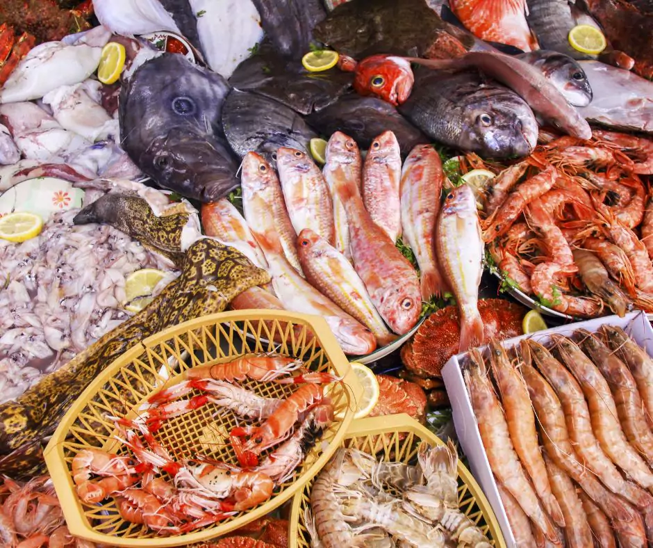 A vibrant seafood display at Joe Patti’s Seafood Market in Pensacola, Florida, showcasing a wide variety of fresh fish, shrimp, lobsters, squid, and other shellfish. The selection includes red mullet, whole fish with glistening scales, tiger prawns, langoustines, and even an eel, all arranged on a bed of ice with garnishes of lemon slices. The assortment highlights the market’s reputation for high-quality, fresh Gulf Coast seafood, making it a popular destination for seafood lovers.