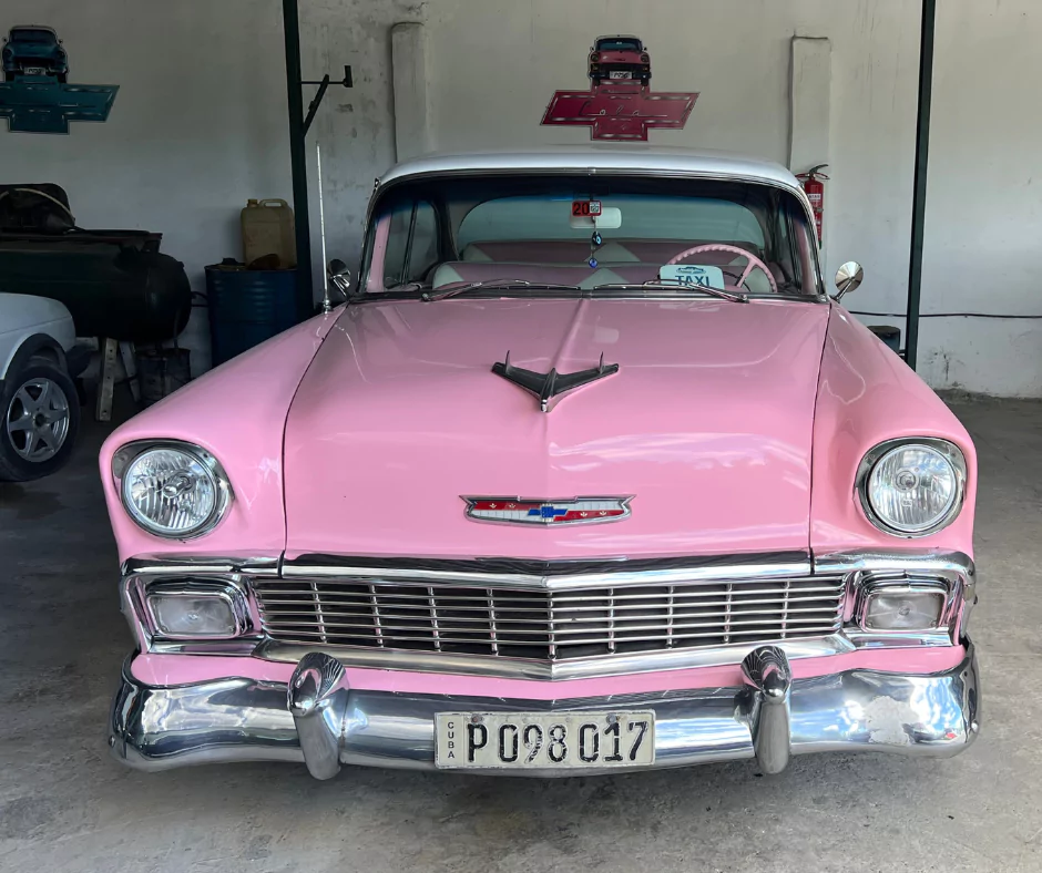 Pink and white 1956 Chevrolet Bel Air classic car parked in a garage in Cuba, used as a taxi.