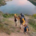 Family of hikers with backpacks climbing mountain against river during trip