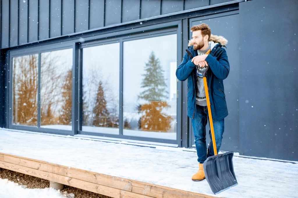 Man with snow shovel near the house in the mountains