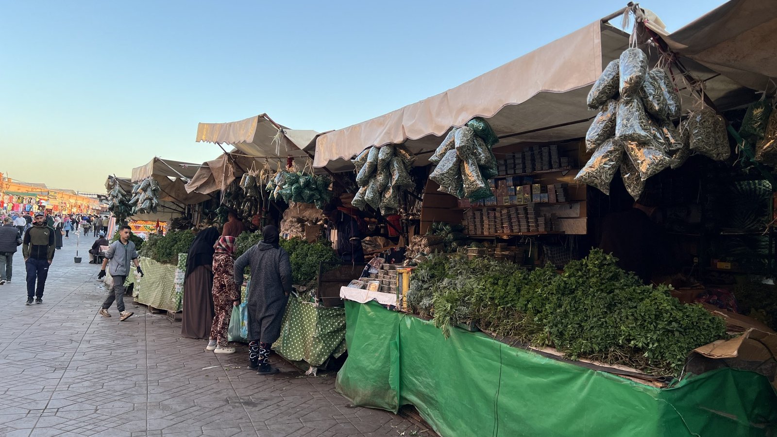 Morning herb and spice stalls at Djemaa el-Fna in Marrakech, with vendors setting up and people walking through the square before it gets busy.