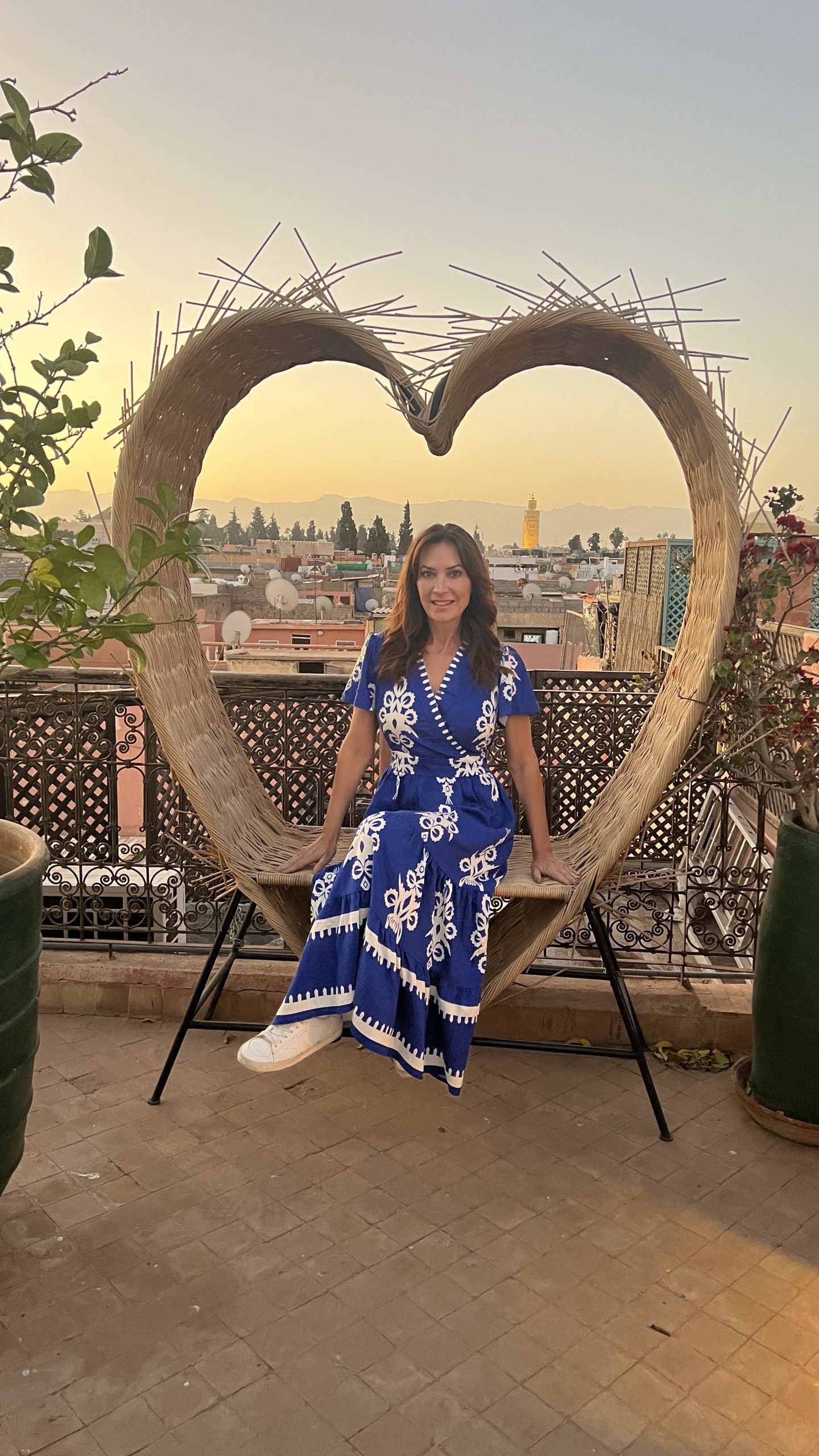 Woman sitting on a rooftop swing chair at sunset in Marrakech with city views and Koutoubia Mosque in the distance during a 2 day in Marrakech trip.