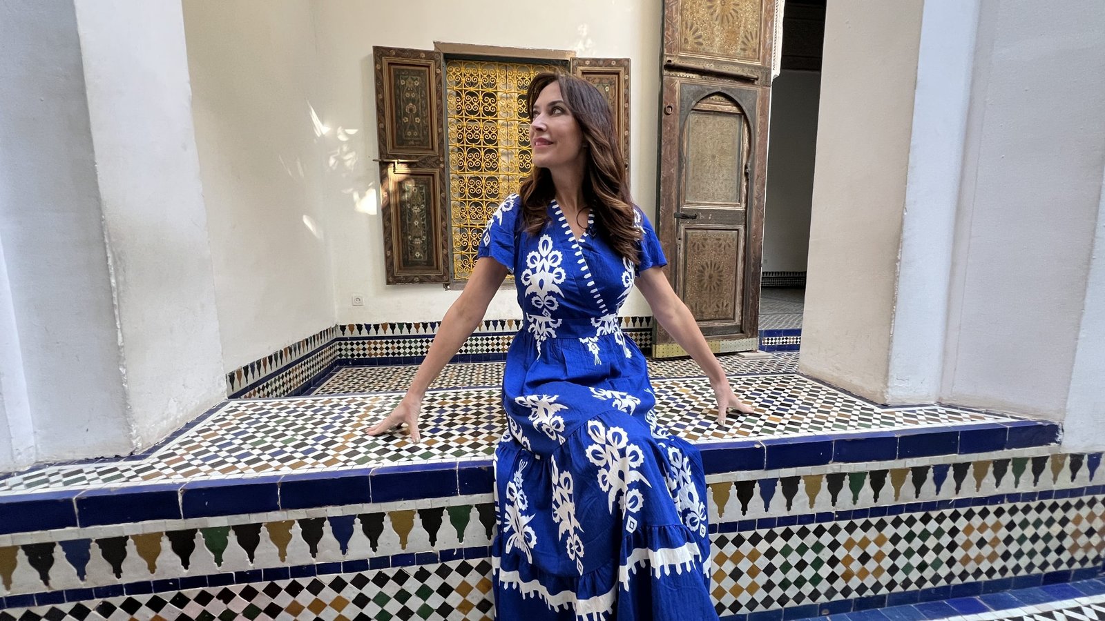 Woman in a blue dress sitting on colorful tiled bench inside Bahia Palace in Marrakech, a photogenic stop during a 2 day in Marrakech visit.