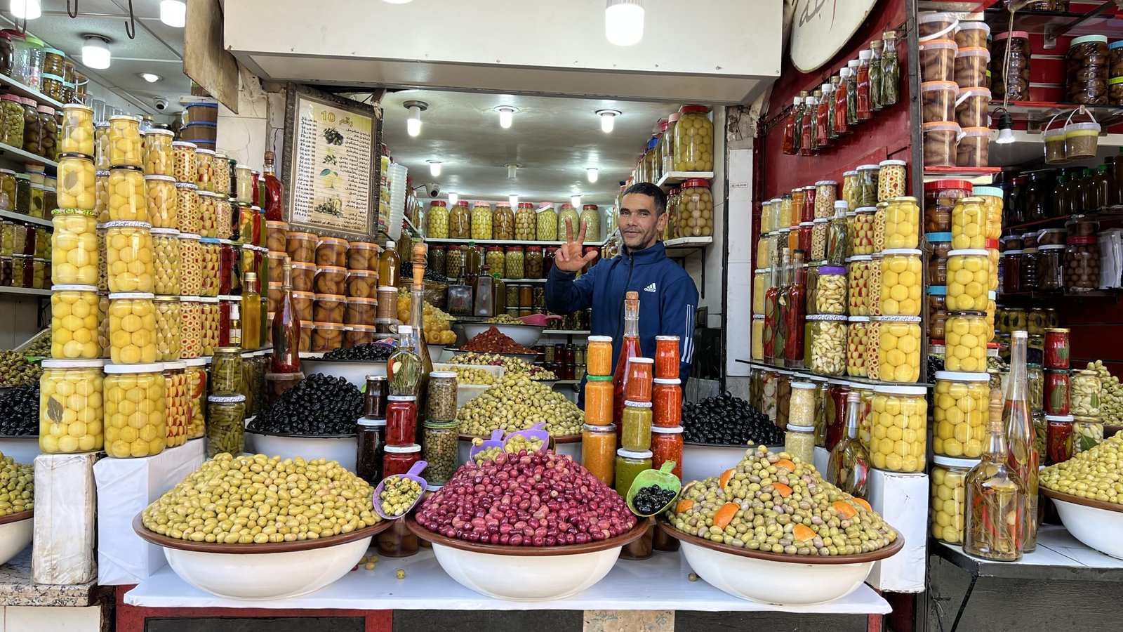 Smiling vendor at an olive and pickle stall in a Marrakech souk, surrounded by colorful jars and bowls often seen during a 2 day in Marrakech market visit.