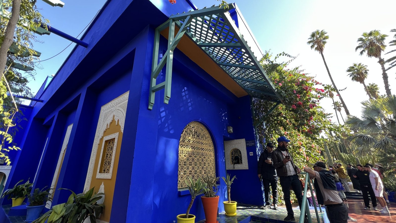 Tourists walking near vibrant cobalt blue walls and decorative arches at Jardin Majorelle in Marrakech, a top attraction during a 2 day in Marrakech itinerary.
