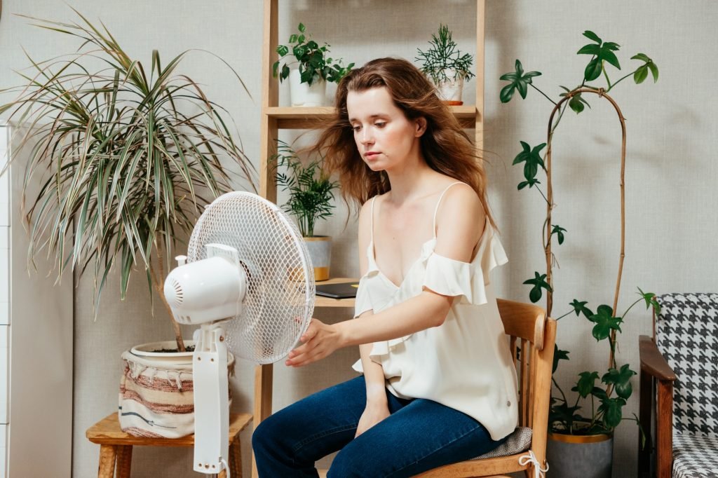 electric fan cools exhausted Caucasian woman languishing in summer heat