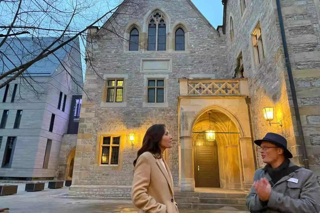 Karen LeBlanc speaking with a local guide outside the historic Augustinian Monastery in Erfurt, Germany, where Martin Luther once lived and studied, with Gothic stone architecture warmly lit in the early evening.