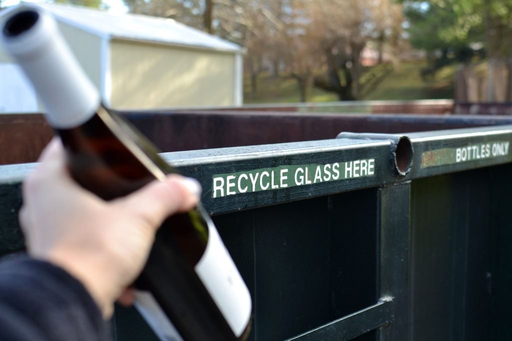 Hand putting a glass bottle in a recycling container dumpster. Recycle glass here.