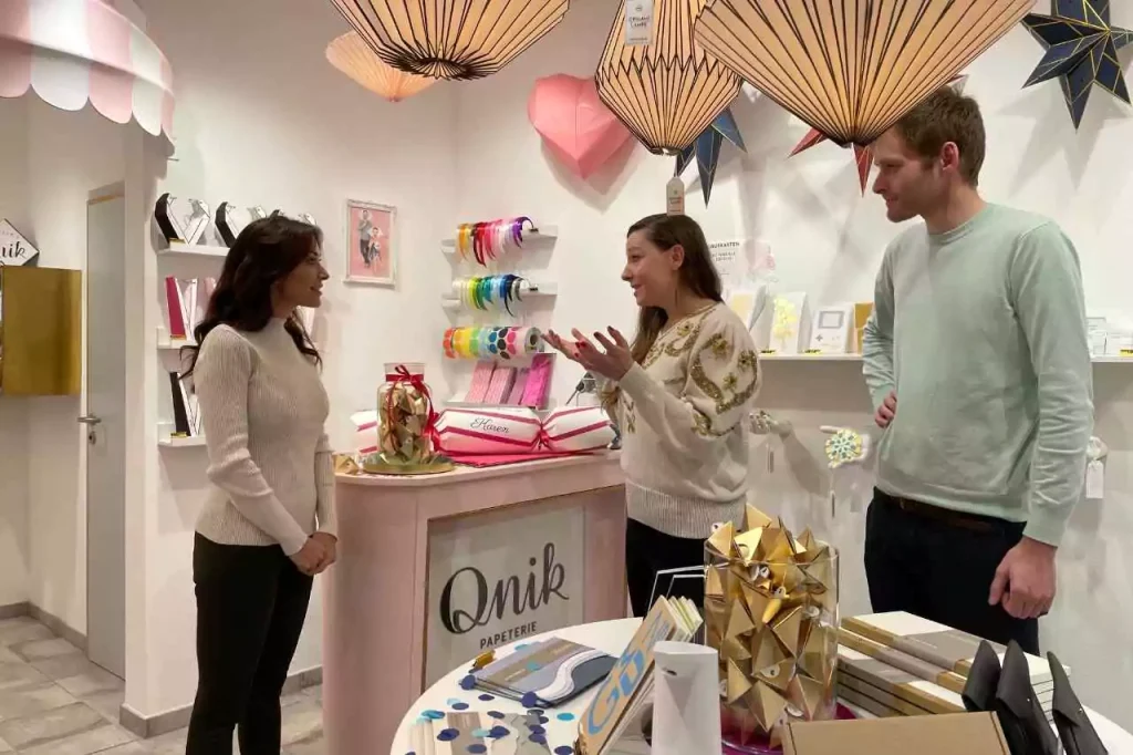 Karen LeBlanc chatting with the creators of Qnik Papier in Erfurt, Germany, surrounded by handmade paper decorations, gift wrap, and creative stationery designs.