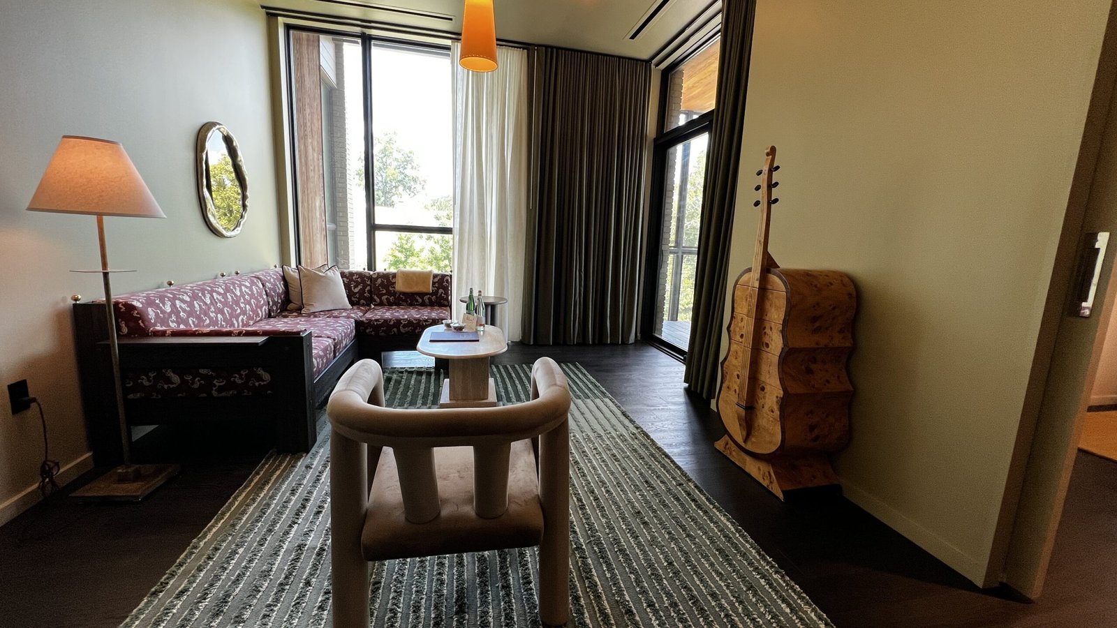 Suite living room at Hotel Saint Augustine featuring sculptural furniture, large windows, and a cello-shaped wooden cabinet.
