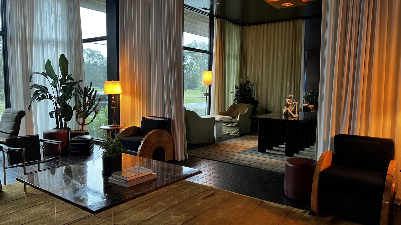 Stylish hotel lobby at Hotel Saint Augustine in Houston with sculptural seating, potted plants, floor-to-ceiling curtains, and warm lighting.