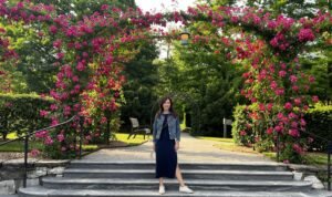 Woman posing beneath a blooming rose-covered archway on stone steps at Longwood Gardens