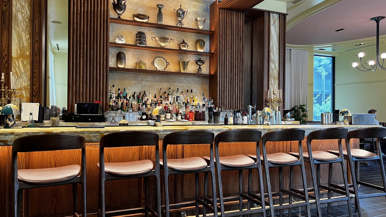 Elegant bar at Perseid restaurant inside Hotel Saint Augustine, with wood accents, backlit shelves, and a marble counter.