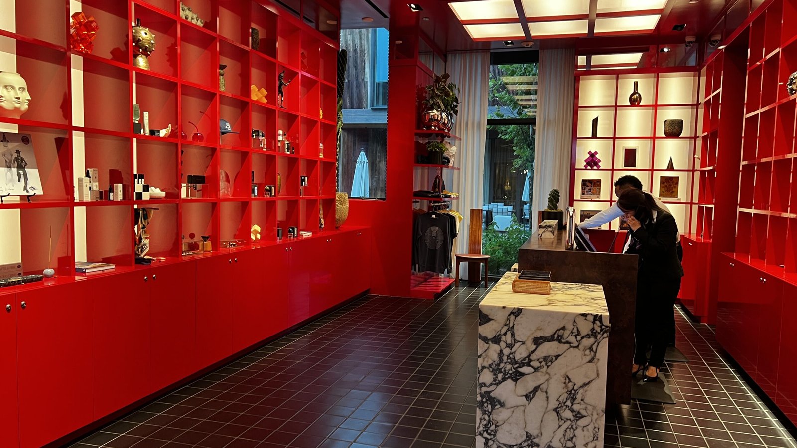 Vibrant red-lacquered lobby at Hotel Saint Augustine featuring floor-to-ceiling shelving with art objects and a marble reception desk.