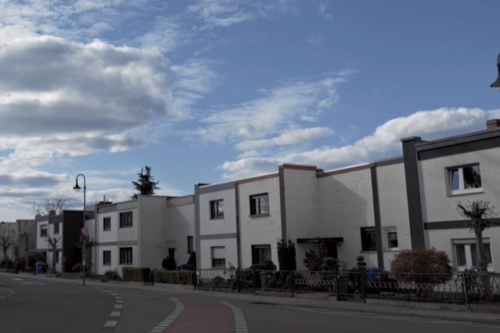 Daytime view of the Törten Housing Settlement in Dessau, showcasing a row of flat-roofed, minimalist Bauhaus-style homes with clean lines and white facades.