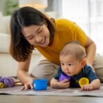 A woman is playing with a baby on the floor. The baby is holding a blue and purple toy